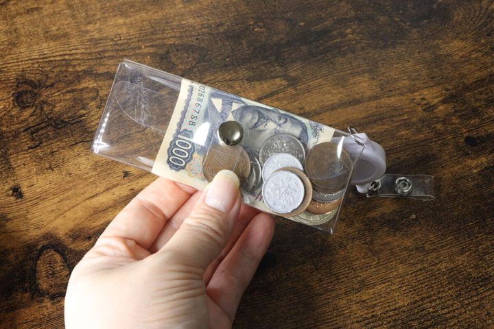 女性の手が透明ポーチを持ち、三つ折りの千円札と小銭が入っている様子