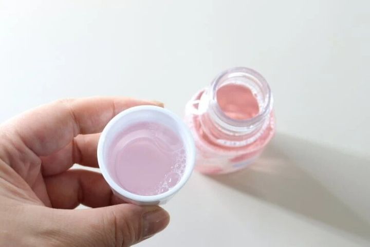 手に持ったコップにピンク色のマウスウォッシュが入っている