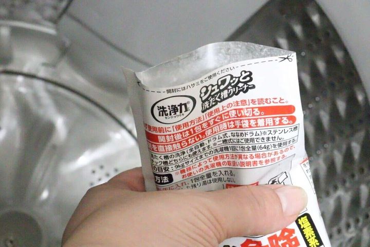 洗濯槽の縁に洗たく槽クリーナーの袋を傾けている手元