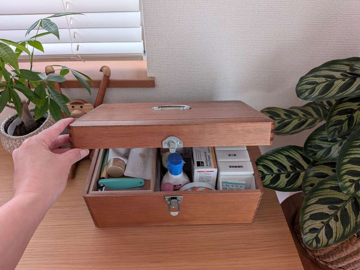 女性が木製救急箱の蓋を開け、中には薬や化粧品
