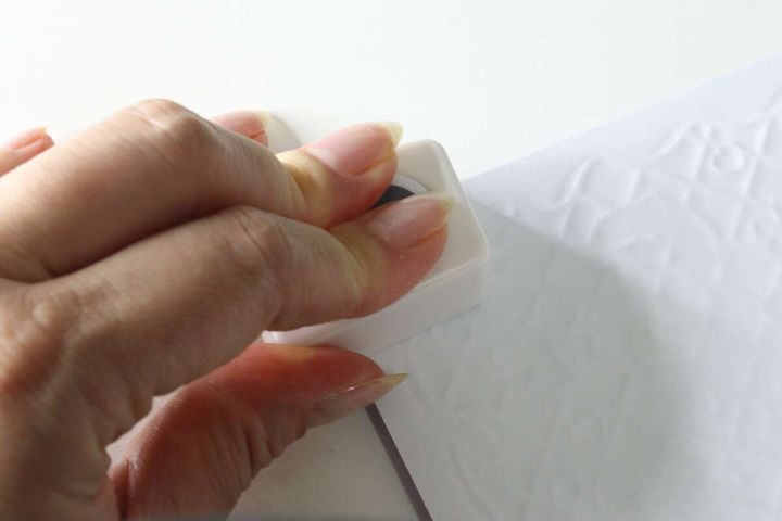 女性の手が白いクラフトパンチを白い紙に押し当てて、紙を切り抜こうとしている様子