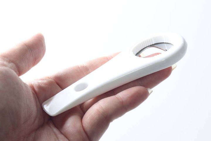 女性の右手が白いオープナーのギザギザ部分を持つ