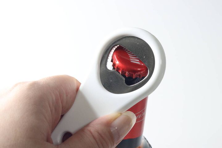 白いオープナーで赤い瓶の王冠を開けようとしている