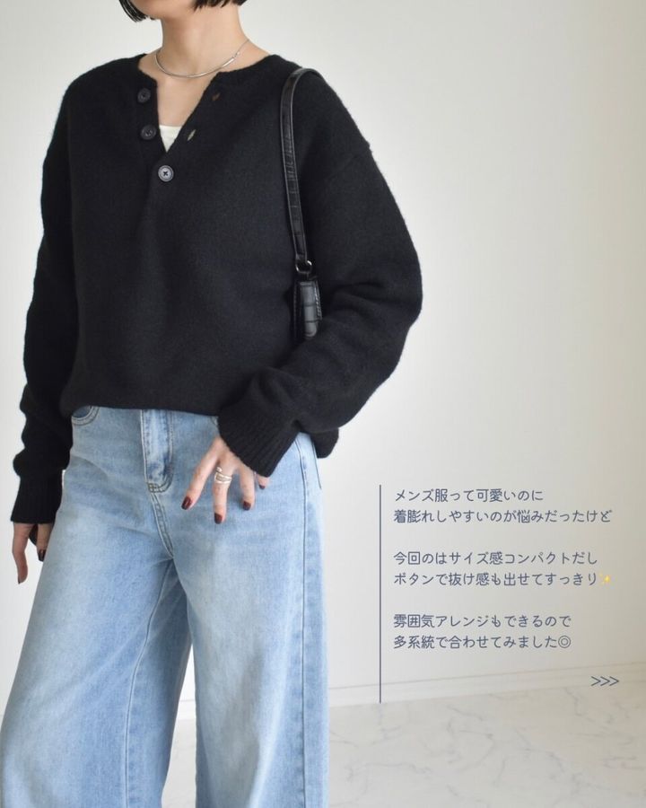 黒いヘンリーネックニットとワイドデニムを着用しポーズをとる女性