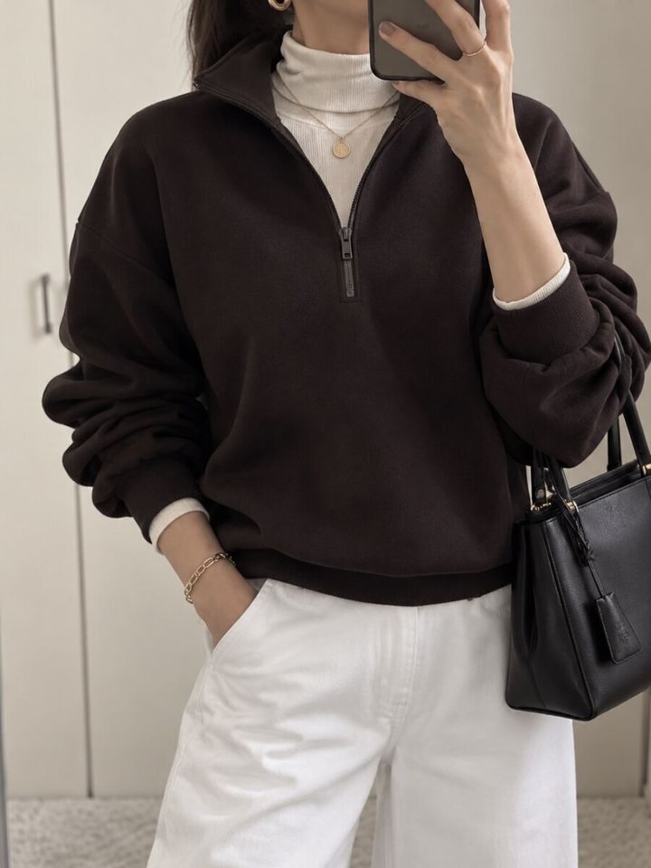 ダークブラウンのハーフジップスウェットを着た女性がスマホを持つ