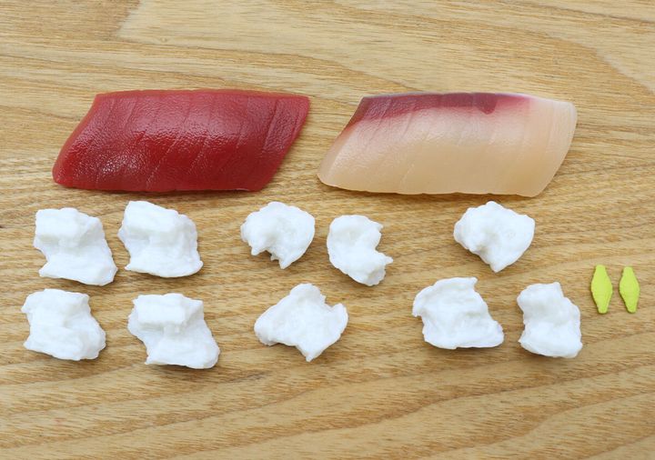 木目のテーブルに、まぐろとはまちのネタ、組み立て前のシャリ、わさびの全パズルパーツ