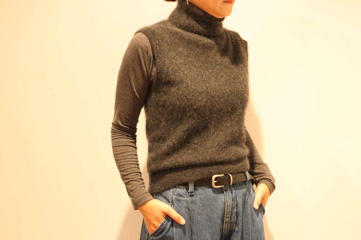 ダークグレーのベストとデニムを着用しポーズをとる女性