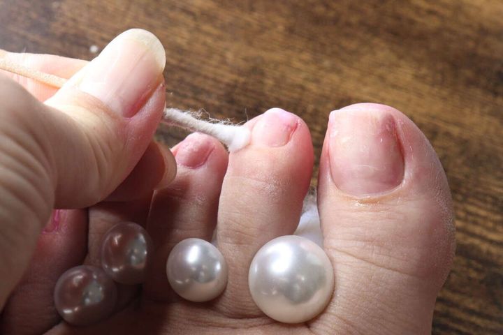 コットンを巻いたウッドスティックで足の甘皮を押し上げている手元