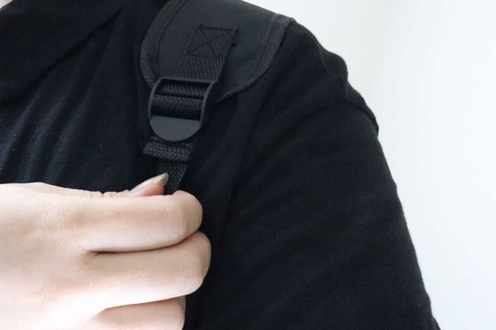 黒い服を着た人がリュックのショルダーベルトを肩にかけ、長さを調整している