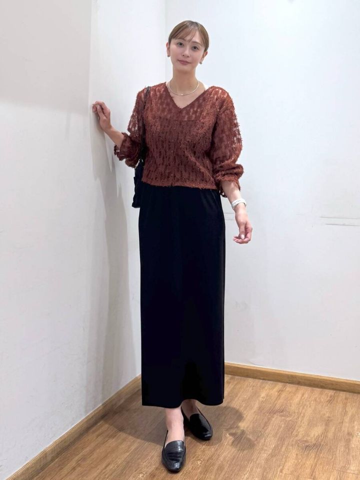 茶色のシアーフリンジトップスと黒スカートの女性