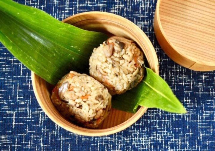 竹製の器に笹の葉を敷き、かしわ飯のおにぎりが2つ並べられている