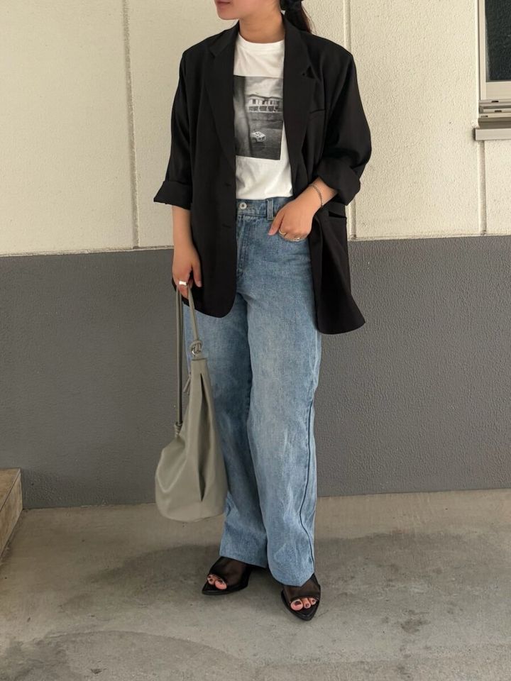 黒のテーラードジャケットの袖をたくし上げ、フォトTとデニムを合わせた女性