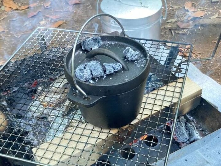 網の上で炭を乗せたダッチオーブンが調理されている