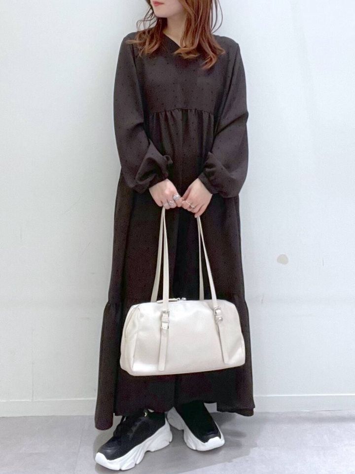 黒いドット柄ワンピースを着て白いボストンバッグを持つ女性