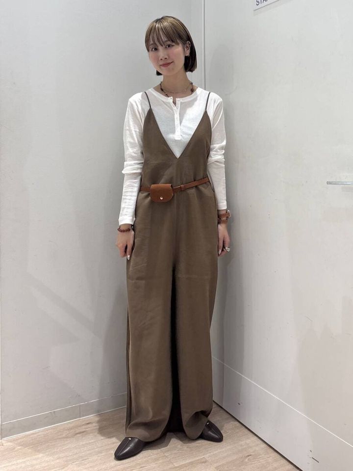 白いトップスと茶色のキャミサロペットを着てポシェットをつけた女性