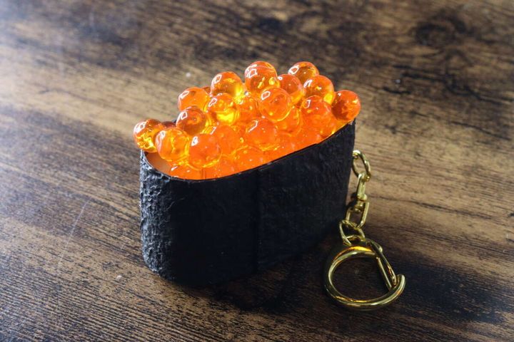 木目調のテーブルに置かれたいくらの軍艦巻きキーホルダー