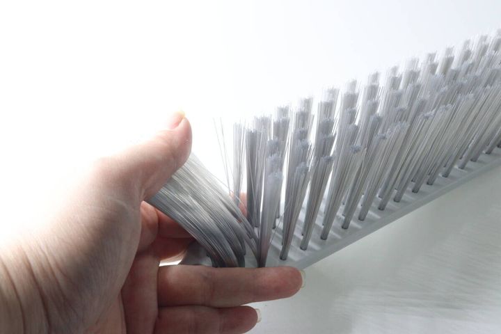 女性の手が、ほうきの白いブラシ部分を指で弾いてコシを確認している様子