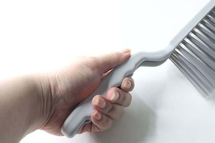 女性の手が、グレーの波形グリップのほうきを握っている様子