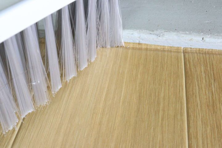 ほうきのブラシ部分が、フローリングの床と壁の境目のゴミをかき出している様子