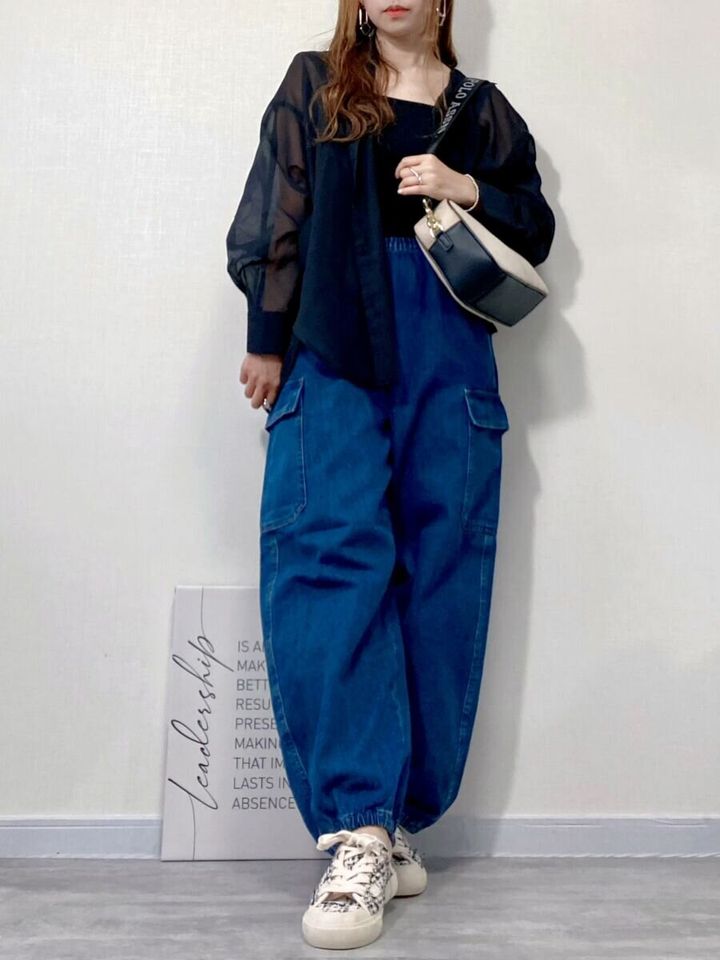 黒のシアーシャツとタンクトップにブルーのデニムカーゴパンツを合わせた女性
