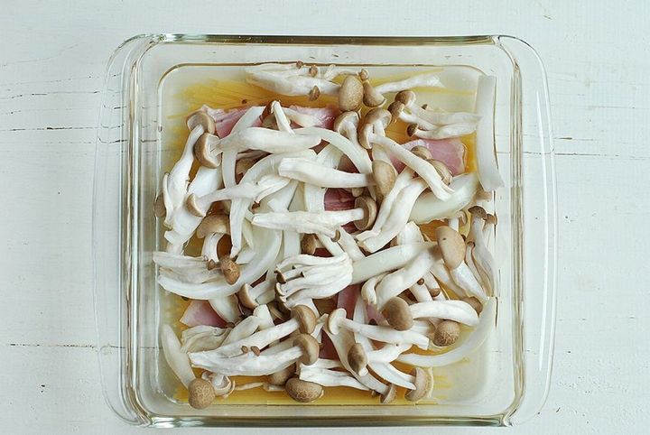 耐熱容器に折ったパスタ、ベーコン、玉ねぎ、しめじを重ねて入れている。