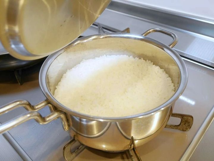 ガスコンロの上で炊飯鍋の蓋を開け炊き上がった白いご飯