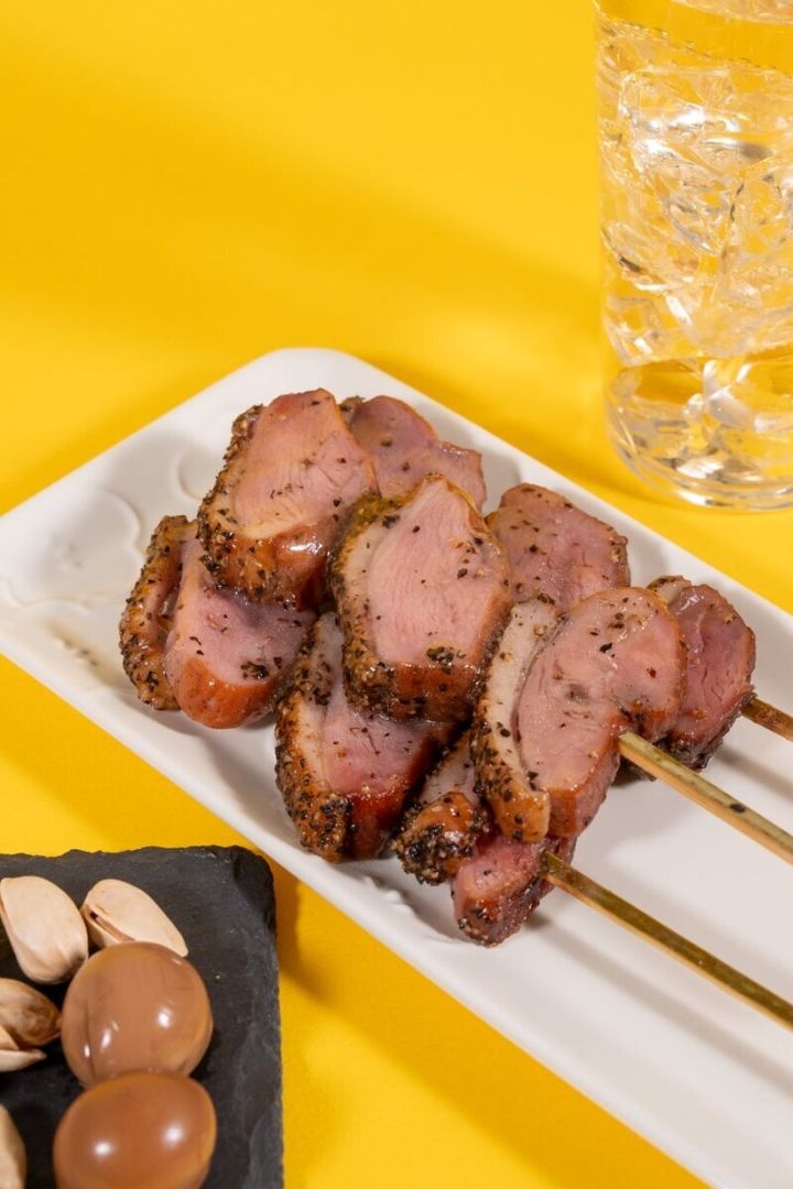 黄色い背景に盛り付けられた燻製あい鴨ロース串と飲み物