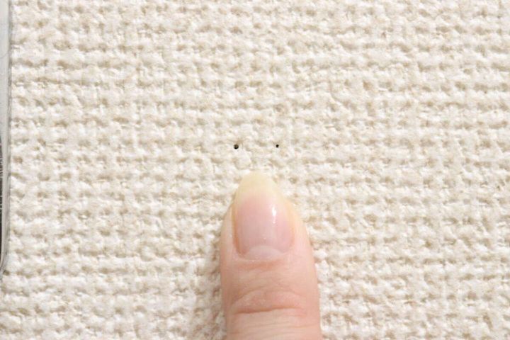 女性の指が壁に残った小さなピン穴を指し示している