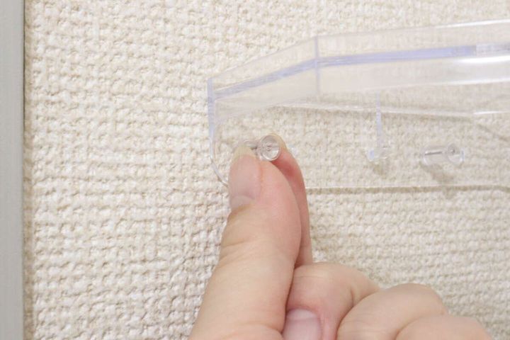女性の指が壁にクリアラックをスリムプッシュピンで固定している