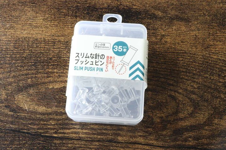 透明なケースに入ったスリムプッシュピンが木目のテーブルに置かれている