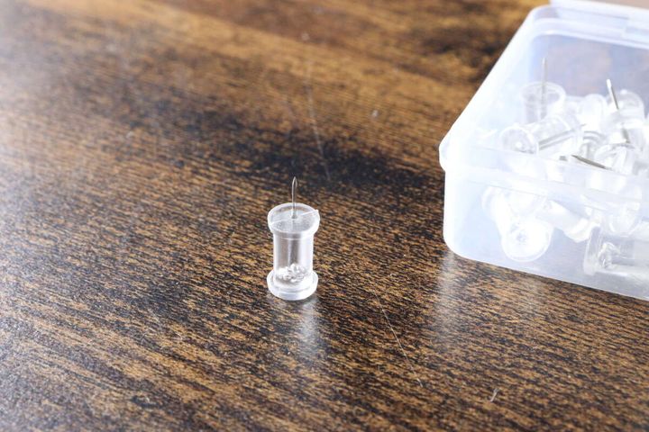 木目のテーブルにスリムプッシュピンが1本とケースが置かれている