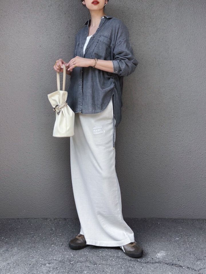 グレーデニムシャツと白スカート、白い巾着バッグの女性