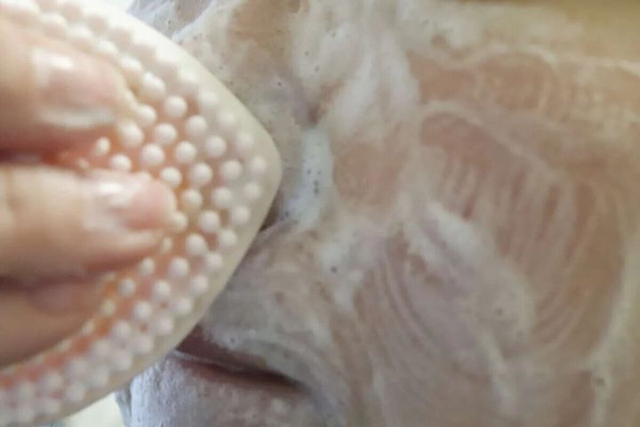 泡立てた顔にハート型洗顔ブラシを当てて洗顔している