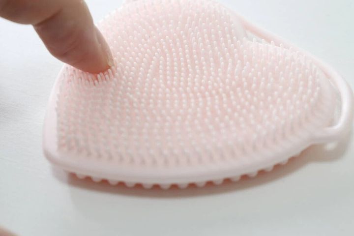 ピンク色のハート型洗顔ブラシの細かい突起を指で触っている