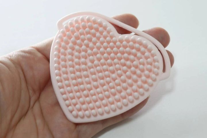 ピンク色のハート型洗顔ブラシを手のひらに乗せている