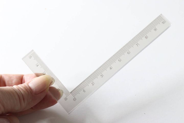L字型のクリアなスタンプ定規を指で持っている