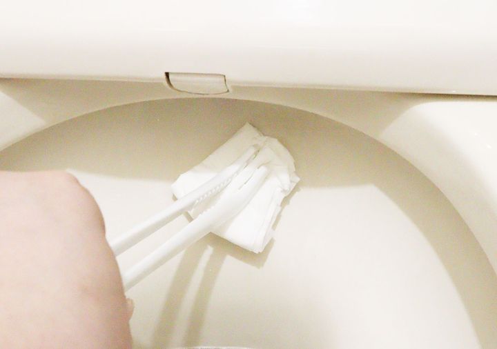 トングでつかんだティッシュでトイレ掃除をしている