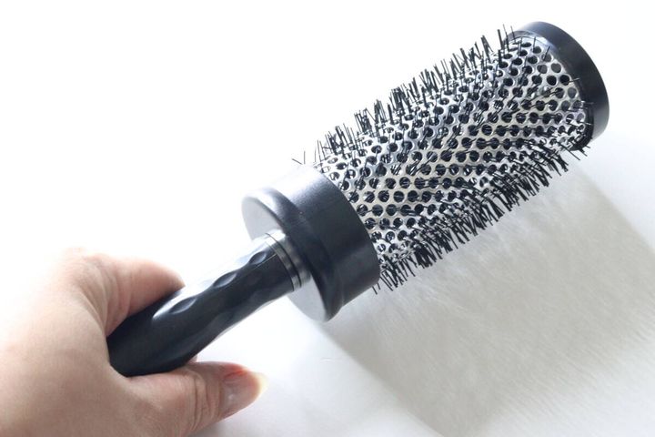 女性が黒いロールヘアブラシを手に持っている様子