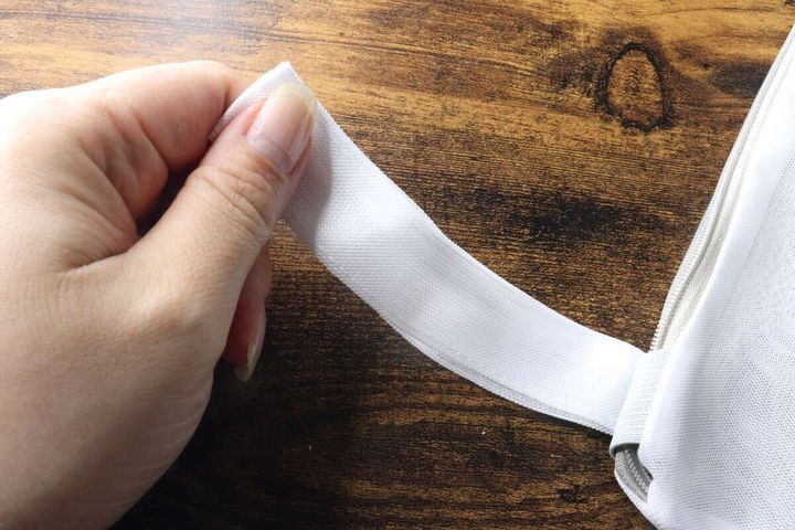 女性の手が白い洗濯ネットの吊り下げループをつまんで見せている