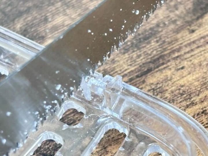 のこぎりで透明なプラスチック製カゴを切断している様子