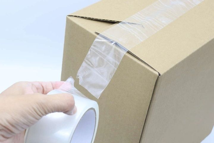 手で梱包用テープを段ボールに貼っている様子