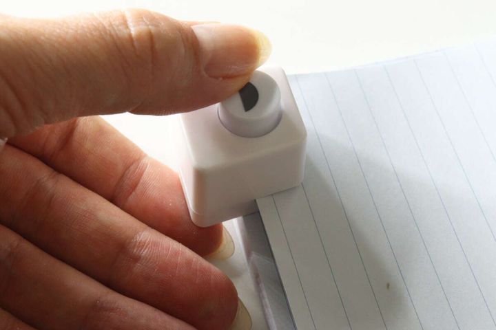 ノートの端にインデックスパンチをセットし、指で押している様子