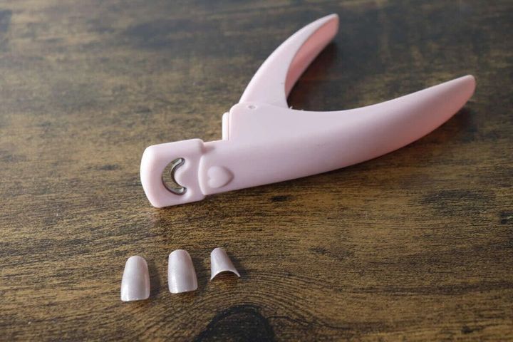 ピンク色のネイルクリッパーとカットされたネイルチップが木製テーブルに置かれている