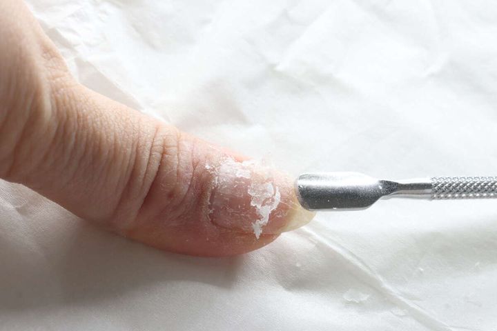指の爪にこびりついたジェルネイルをメタルプッシャーで削り取っている様子