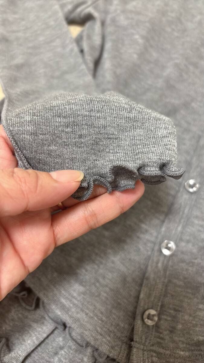 指でつまんで見せるカーディガンの袖口のフリル