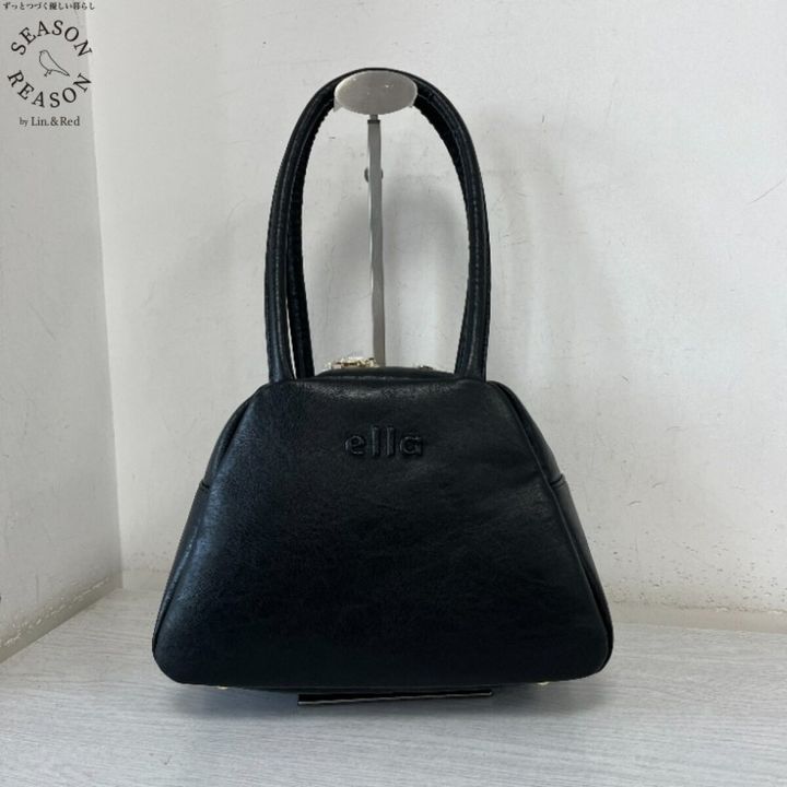 「ella」ロゴ入りの黒いレザー調ボストンバッグが白い台に置かれている