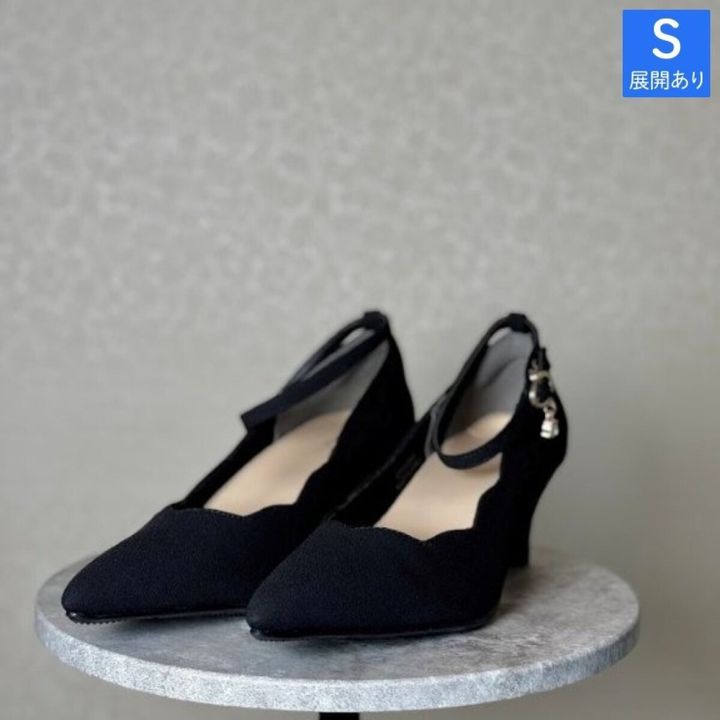 波型カットとストラップ付きの黒いパンプスが台の上に置かれている