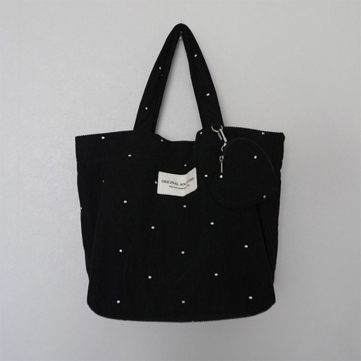 ドット刺繍の黒いトートバッグとハート型ポーチが壁に掛かっている