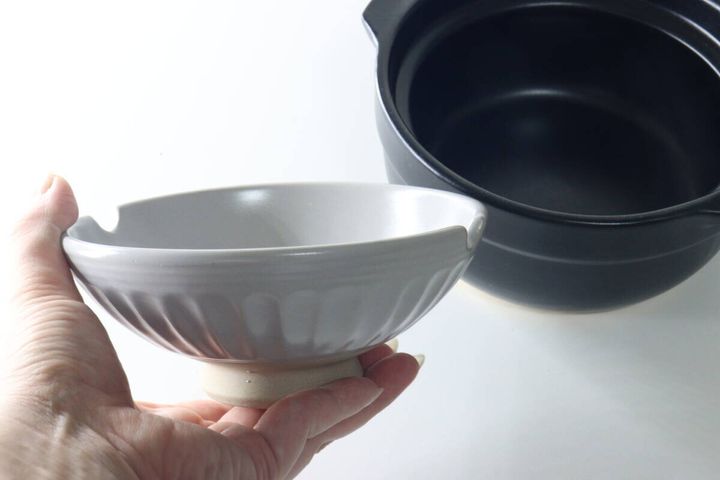 女性の手が、茶碗として使えるグレーの土鍋の蓋を持っている