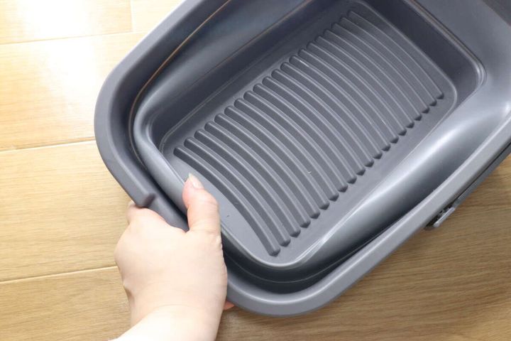 女性の手がたらいを内側に押し込み、折り畳んでいる途中の様子。